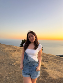 Audrey Wang stands on a hill in from of an ocean at sunset